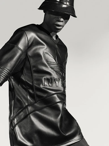 Monochrome studio shot of a Black male model in a black leather Adidas x Ivy Park outfit, including a bucket hat and matching shirt.