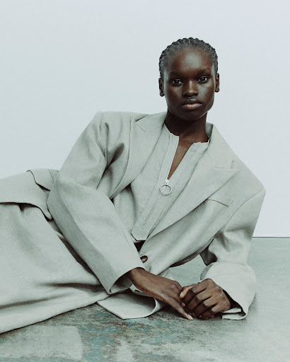 Black woman wearing a grey blazer and matching top lying on the floor against a neutral background.