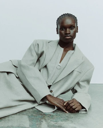 Black woman wearing a grey blazer and matching top lying on the floor against a neutral background.