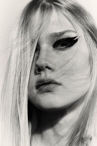 Close-up portrait of a woman with long blonde hair and dramatic black winged eyeliner by Melanie and Ramon.