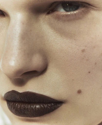 Close-up portrait of an adult female with fair skin and dark lips, featuring defined facial features and a neutral expression.