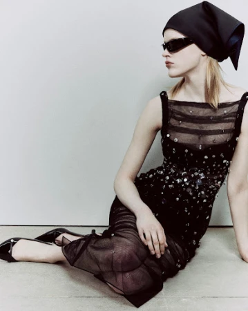 Model seated on the floor wearing a black embellished sheer dress, headscarf, and sunglasses art directed by Melanie and Ramon.