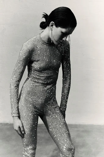 Monochrome fashion shot of a woman in a sparkling jumpsuit, long earrings, and a low ponytail against a neutral backdrop.