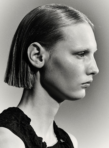 Monochromatic portrait of a young adult woman with a sleek bob haircut, side profile, wearing a dark top, against a neutral background.