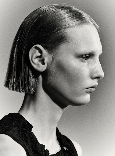 Monochromatic portrait of a young adult woman with a sleek bob haircut, side profile, wearing a dark top, against a neutral background.