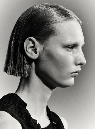 Monochromatic portrait of a young adult woman with a sleek bob haircut, side profile, wearing a dark top, against a neutral background.