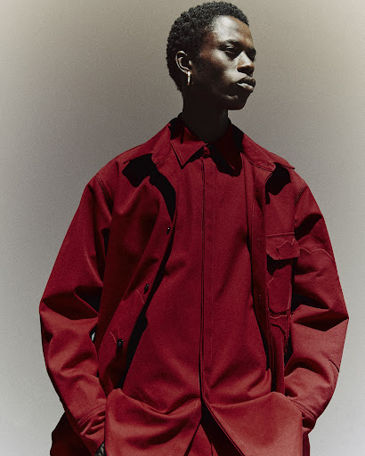 Studio portrait of a Black male model wearing a red-burgundy collared shirt and matching pants against a neutral backdrop.