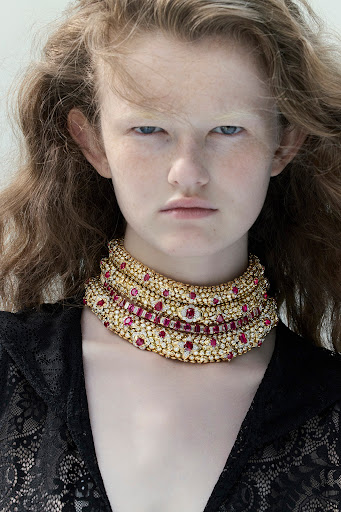 Close-up portrait of a model wearing an elaborate jewelled gold choker necklace and black lace top
