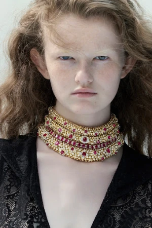 Close-up portrait of a model wearing an elaborate jewelled gold choker necklace and black lace top