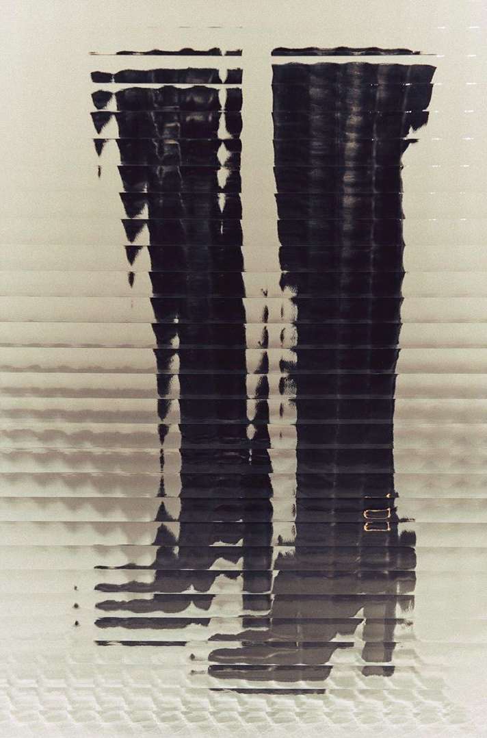 Graphic image of a pair of dark-colored, shiny boots with buckle detail, presented in a horizontally-striped, abstract, and somewhat blurred style.