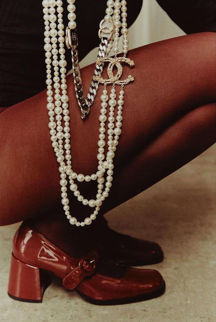 Fashion shot featuring a woman's legs, wearing red tights and red patent leather Mary Jane shoes. She is accessorized with layered pearl necklaces.