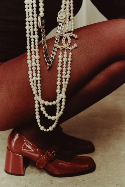 Fashion shot featuring a woman's legs, wearing red tights and red patent leather Mary Jane shoes. She is accessorized with layered pearl necklaces.