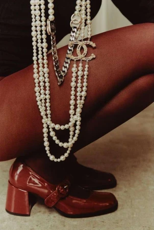 Fashion shot featuring a woman's legs, wearing red tights and red patent leather Mary Jane shoes. She is accessorized with layered pearl necklaces.