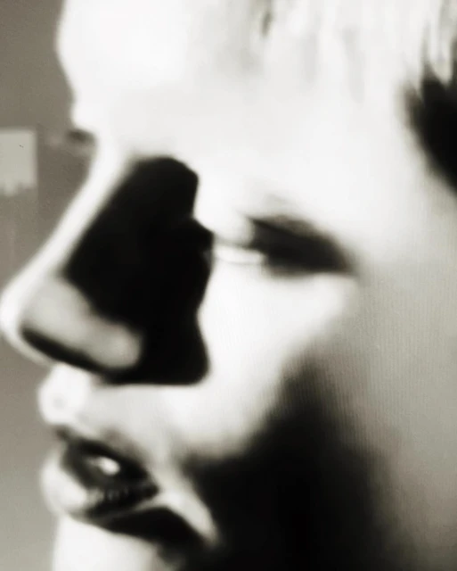 Close-up profile of a person's face with dark and light shadows, focusing on the nose, mouth, and cheekbones.