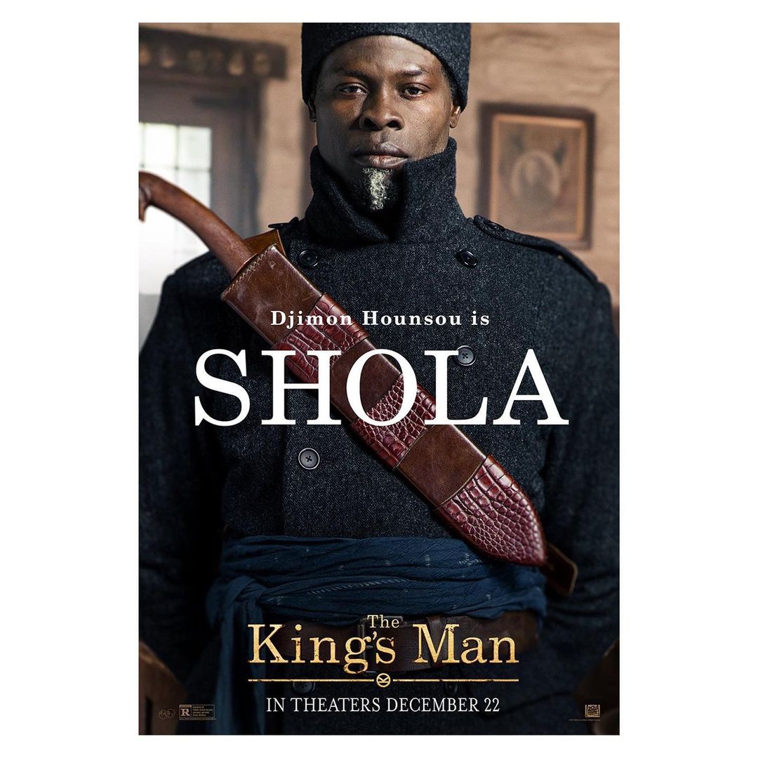 Movie poster featuring Djimon Hounsou as Shola in The King's Man. He is wearing a wool coat, black cap, and a leather sword holder.