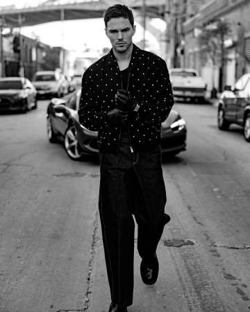 Monochrome portrait of a man in a polka dot jacket walking on a city street with cars and buildings in the background.