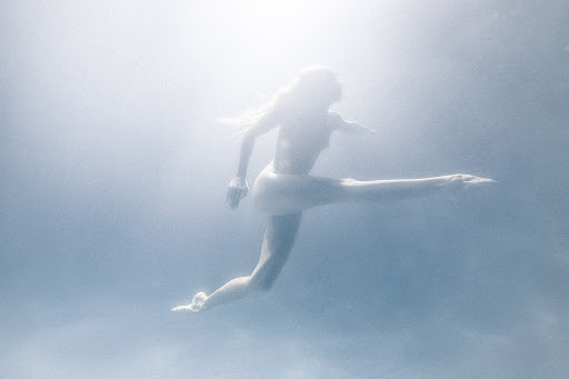 Underwater action shot of a woman swimming with extended limbs in a blurred blue-toned environment, capturing a sense of movement.