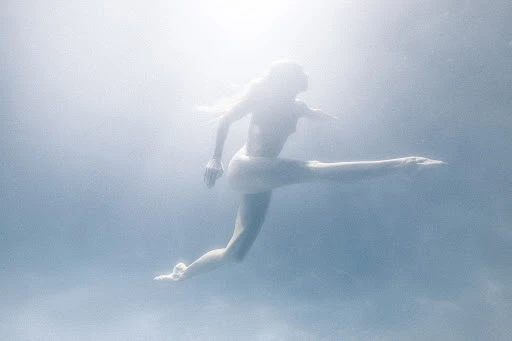 Underwater action shot of a woman swimming with extended limbs in a blurred blue-toned environment, capturing a sense of movement.