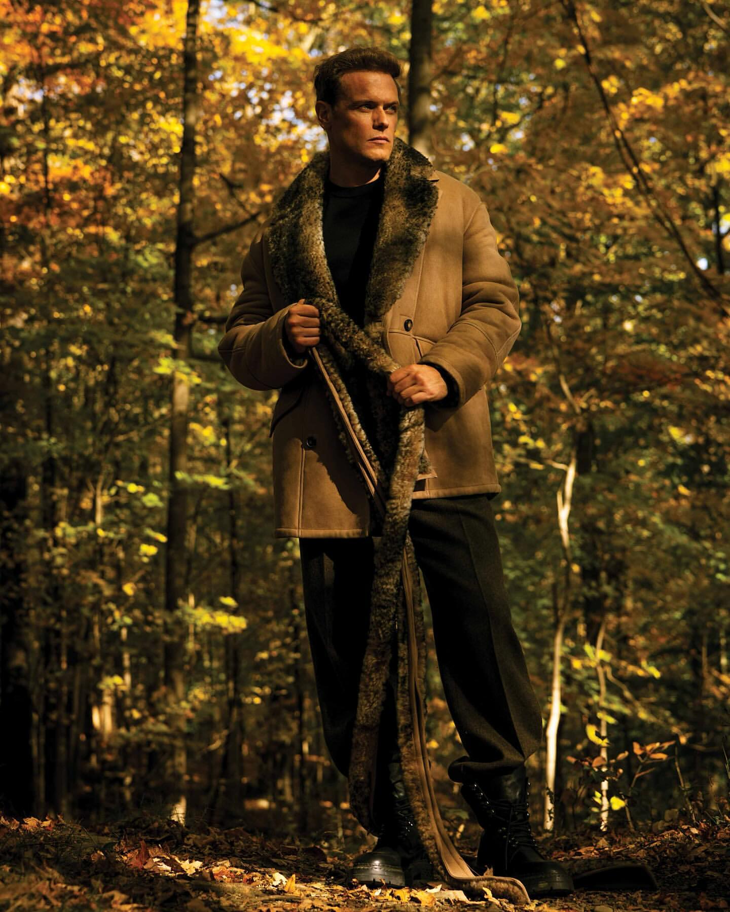 Man in coat with fur collar posing in a forest. Autumn foliage and bare trees in the background. Fashion, portrait, outdoor.