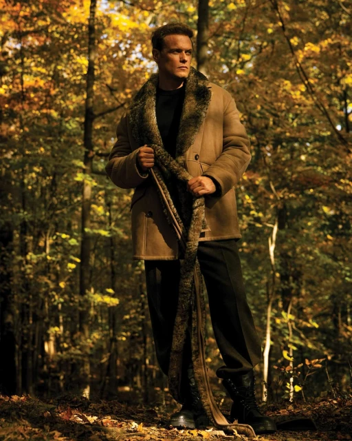 Man in coat with fur collar posing in a forest. Autumn foliage and bare trees in the background. Fashion, portrait, outdoor.