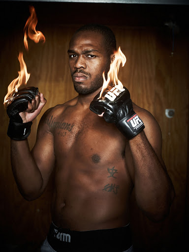 Portrait of Jon Jones holding his hands up with flames rising from his UFC gloves against a wooden background