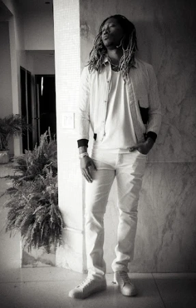 Monochrome portrait of Future with dreadlocks leaning against a marbled wall, wearing a light jacket, t-shirt, and pants.