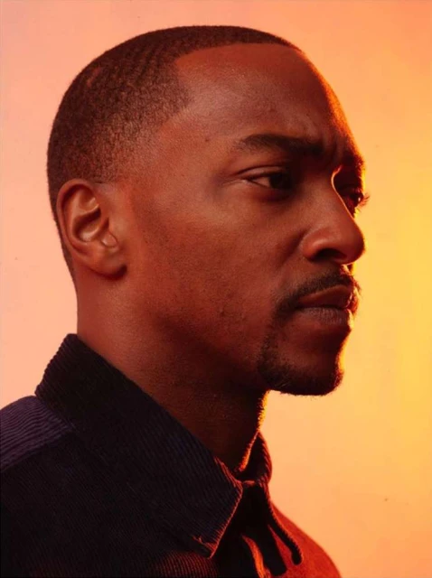 Portrait of a handsome adult male with short dark hair and a slight mustache, wearing a blue corduroy shirt against an orange background.