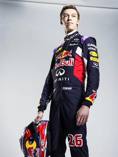 Race car driver in uniform holding helmet, standing in front of a white wall in a photo studio with a full body shot.