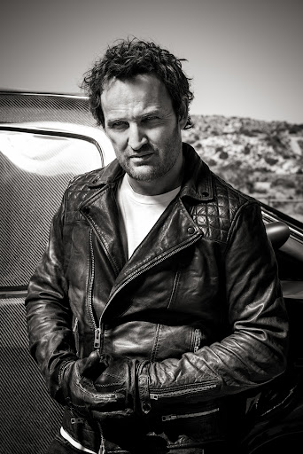 Portrait of a man in a quilted leather jacket standing outdoors by a vehicle