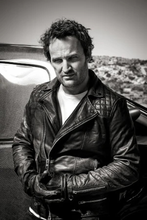 Portrait of a man in a quilted leather jacket standing outdoors by a vehicle