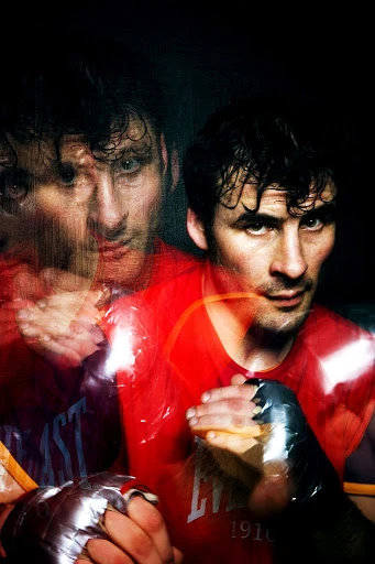 Boxer portrait with motion blur effect, wearing red top and boxing gloves in dark environment with a vintage tone, serious expression.