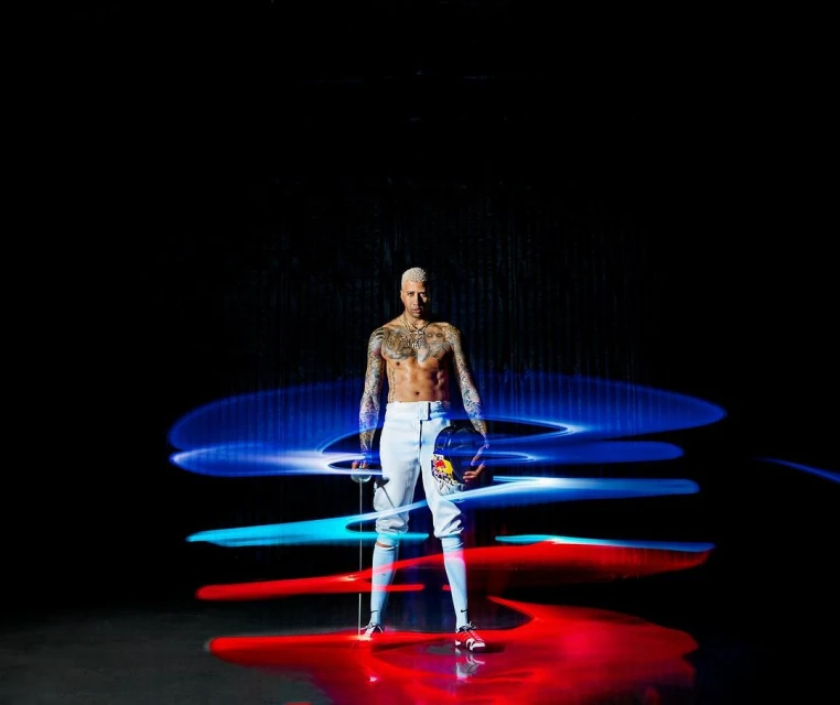 An athletic, shirtless man stands centered, holding a fencing mask and sword against a black background with red and blue light trails.