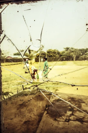 Cracked glass window with an outdoor view of three adults in casual clothing on a grassy lawn near trees and a residential structure.