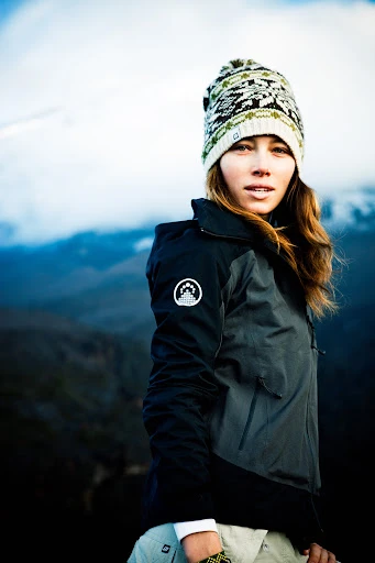 Jessica Biel wearing a patterned beanie hat and black outdoor jacket against a mountain landscape by Michael Muller