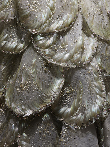 Detailed macro shot of beaded and feathered couture dress with iridescent sequins and silver embellishments on a tulle base.
