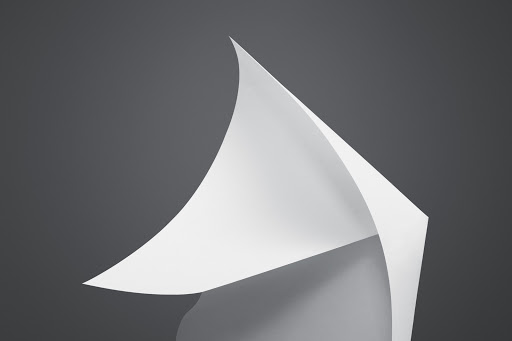 Abstract image of a curved white paper sheet on a gray backdrop, creating a minimalist and clean aesthetic with smooth transitions and shadows.