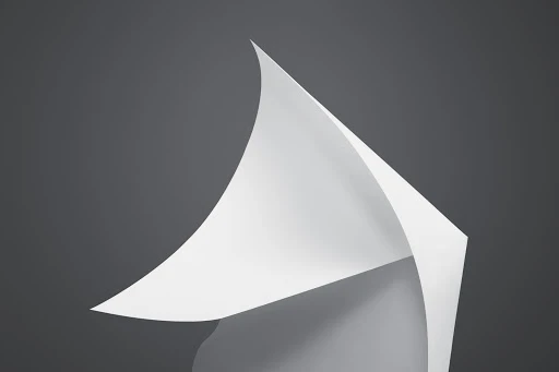 Abstract image of a curved white paper sheet on a gray backdrop, creating a minimalist and clean aesthetic with smooth transitions and shadows.