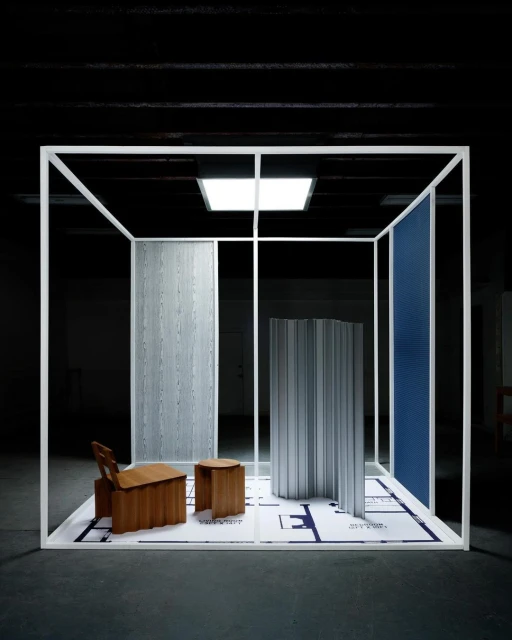 Interior design installation featuring deconstructed furniture pieces, partitions, and a blueprint floor within a white frame structure, indoors.