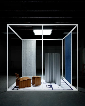 Interior design installation featuring deconstructed furniture pieces, partitions, and a blueprint floor within a white frame structure, indoors.