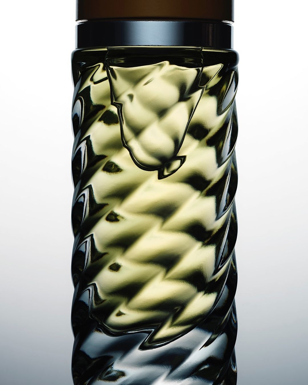Studio shot of a textured glass bottle with a brown top against a white background, highlighting the bottle's design and color.