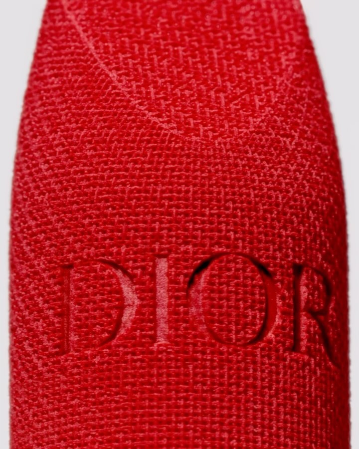 Close-up of a red textured lipstick case with debossed Dior brand logo against a neutral backdrop