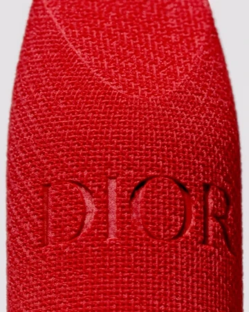 Close-up of a red textured lipstick case with debossed Dior brand logo against a neutral backdrop