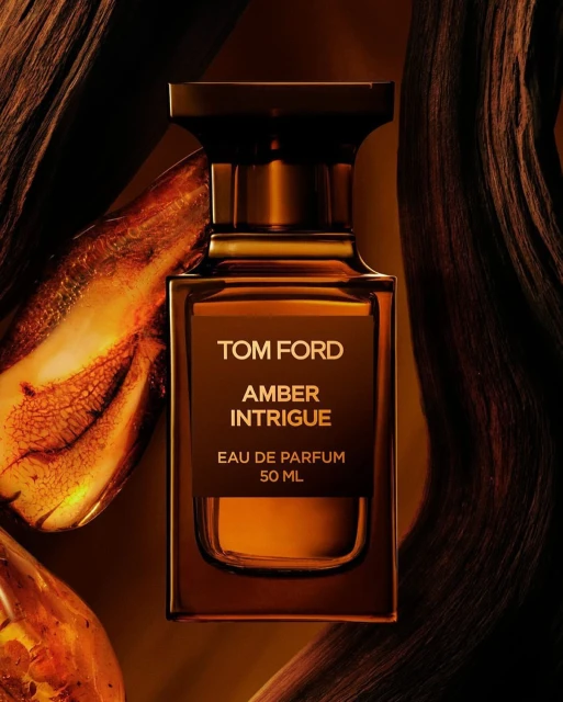 Close-up of a Tom Ford Amber Intrigue Eau de Parfum bottle with amber accents and amber-colored liquid.