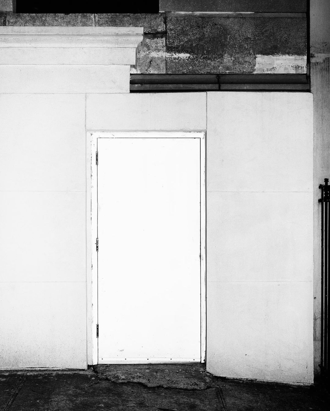 Black and white architectural image featuring a closed white door set into a wall with textured masonry and a dark gray foundation.