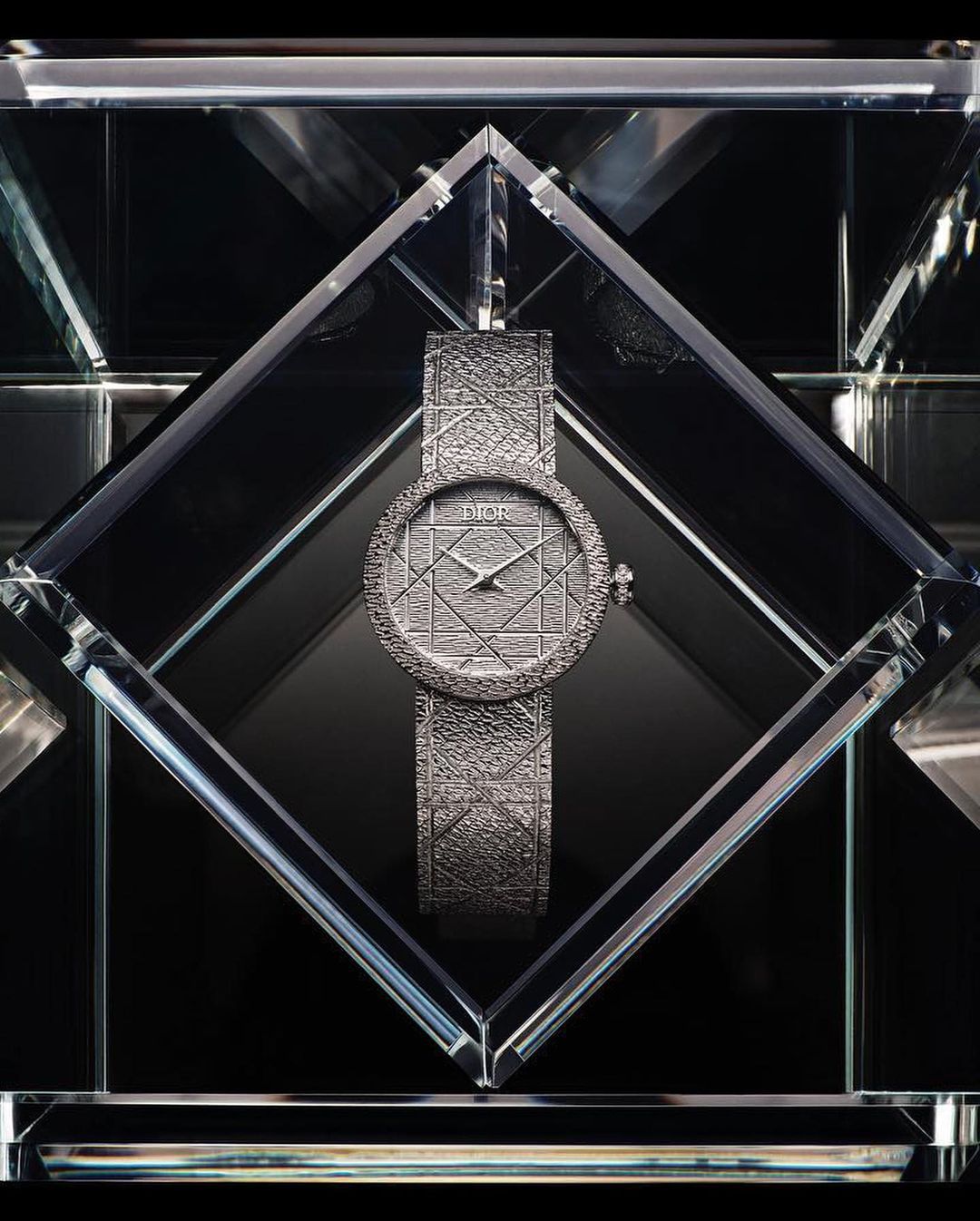 Elegant Dior watch encased in a crystal display, showcasing luxury timekeeping with geometric patterns and a modern aesthetic against a dark backdrop.