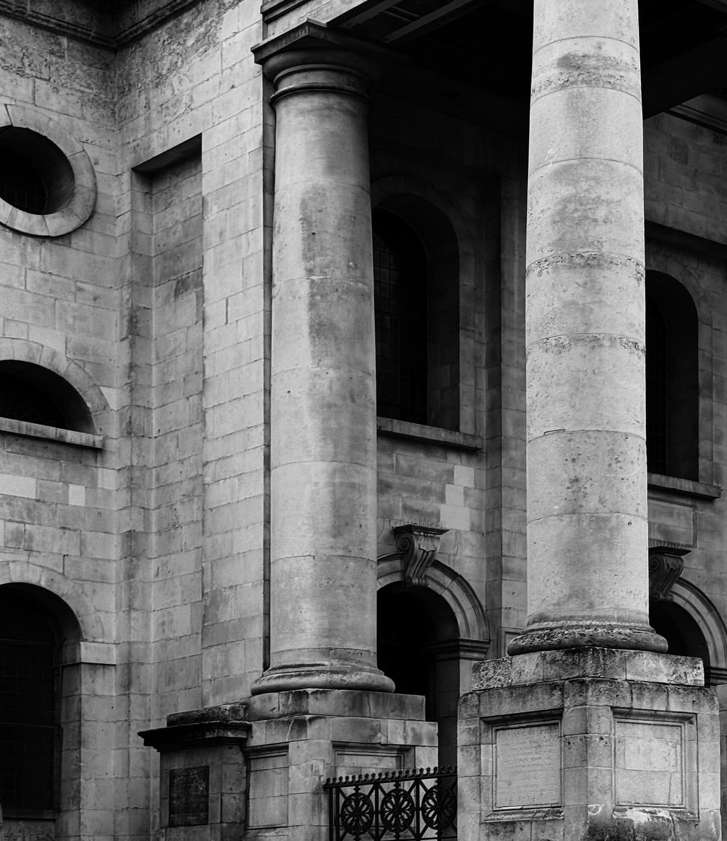 Architectural photography in black and white showcasing the exterior of a stone building with classical columns and arched windows.