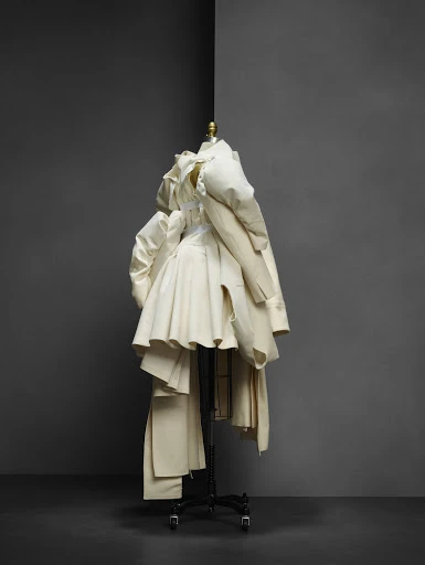 Off-white couture garment displayed on a mannequin in a studio setting, showcasing draping, tailoring, and artistic fashion design.