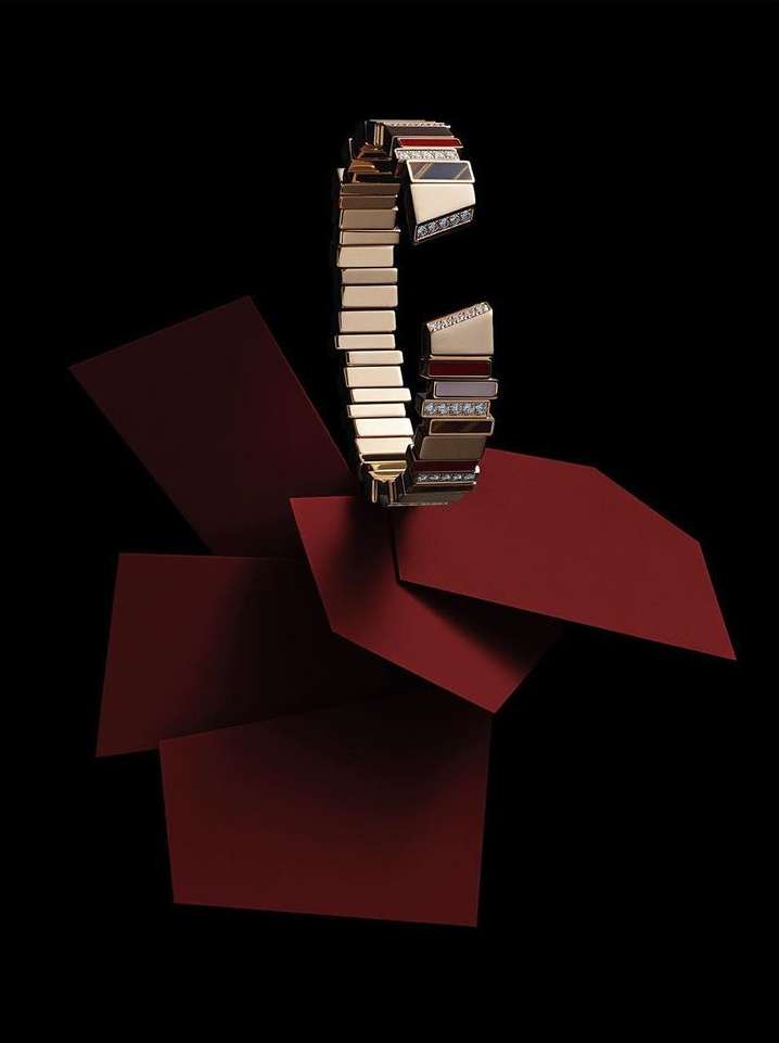 A luxurious gold bracelet with diamond accents is showcased against a backdrop of layered geometric shapes in deep red and black.