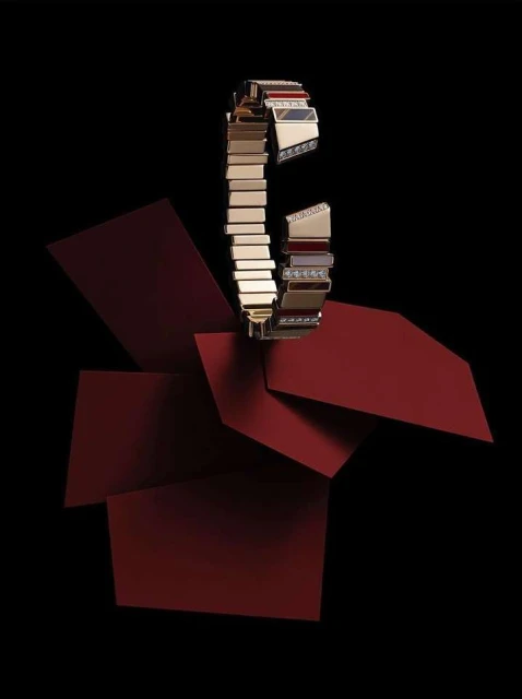 A luxurious gold bracelet with diamond accents is showcased against a backdrop of layered geometric shapes in deep red and black.