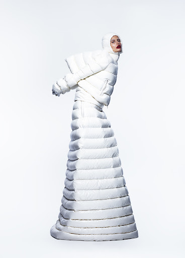 Model wearing a matching white padded puffer jacket and long quilted skirt with a hooded headpiece against a plain white studio background.